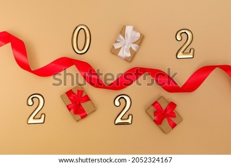 New Year 2022. Top view New Year mockup on beige background: red ribbon, gift box, gold numbers and multicolored sparkles. Layout of postcards, invitations.