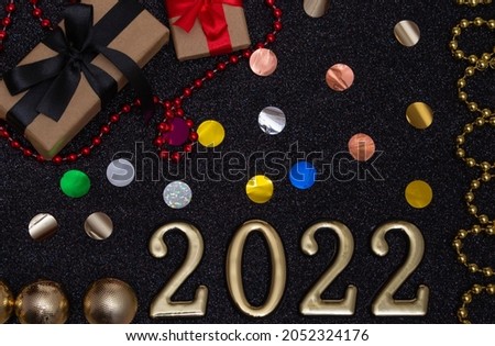 New Year 2022. Top view New Year mockup on black shiny background: red ribbon, gift box, gold numbers and multicolored sparkles. Layout of postcards, invitations.