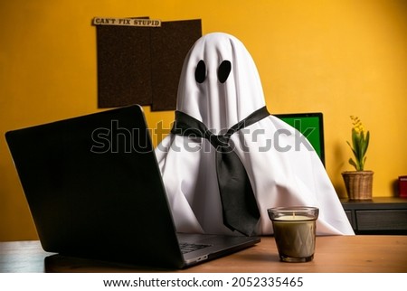 Ghost writing an article on laptop n home office with "can't fix stupid" sign on the wall. Ghostwriter wearing a tie in a desk. Person working or studying in halloween. Green screen computer.