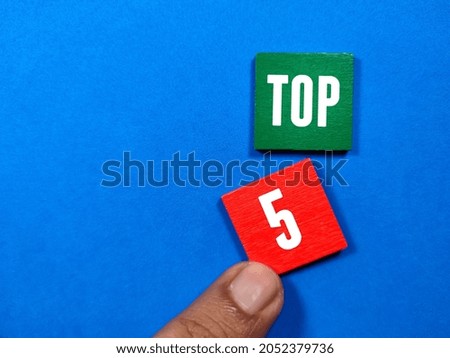 Hand holding a wooden cube with the word Top 5 on a blue background Royalty-Free Stock Photo #2052379736