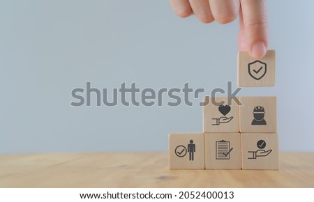 Safety at work concept. Hand holds wooden cube with safety icons; safety first, protections, health, regulations and insurance.  Used for banner, beautiful bright background and copy space. Royalty-Free Stock Photo #2052400013