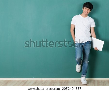 Content Asian male freelancer holding laptop netbook computer and pose with positve and friendly smile standing on green background in studio, teen and tech concept.