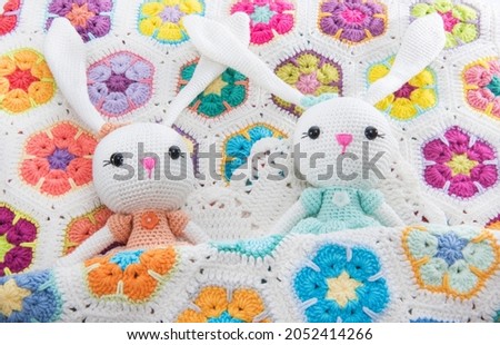Two toy bunnies sleeping in a baby blanket. Rabbit made with colored threads. 