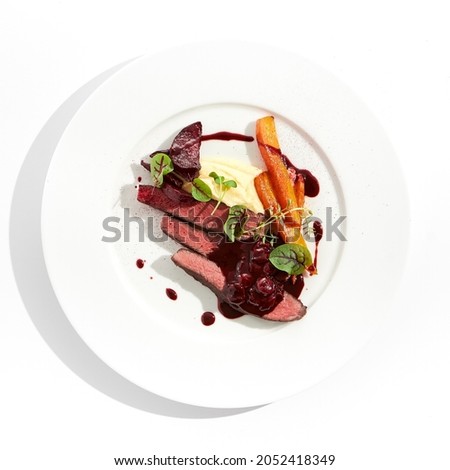 Venison steak with baked vegetables isolated on white plate. Meat steak medium rare roasted with carrot, beetroot and mashed potatoes with cherry sauce. Wild meat in restaurant menu