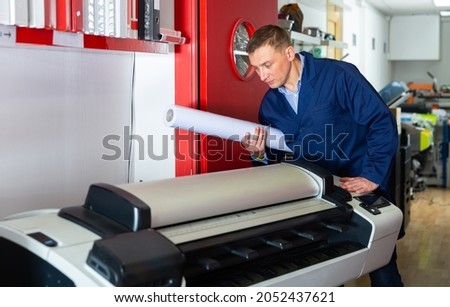 Worker loads new roll of paper into the plotter. High quality photo