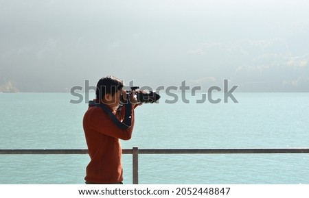 A young Asian man taking pictures by lakeside in Brienz, Switzerland.