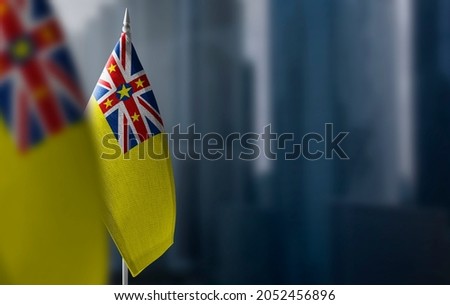 Small flags of Niue on a blurry background of the city