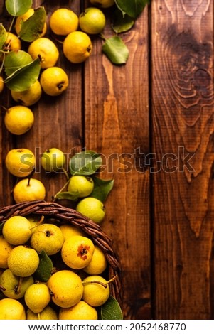 there are a lot of pears on the wooden table. In the middle is a cutting board on which pears are cut into two halves and a knife