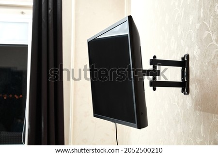 Swivel TV bracket LED display. Side view. X-shaped red fasteners. Black color. Multiplanar. Hangs on a wall. Reliable and comfortable fastening. Childproof and rollover protection. Metallic equipment. Royalty-Free Stock Photo #2052500210