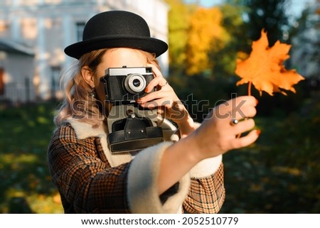Young hipster woman photographing autumn fallen leaf on retro film camera outdoors in sunny weather. Selective focus on girl photographer in boho clothes and hat using vintage camera. Hobby, lifestyle