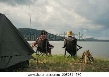 Friendship fisherman or Angler sitting a chair together and camping to fishing at the lake. Camping tent on the shore of the lake. Survival concept. Royalty-Free Stock Photo #2052514760