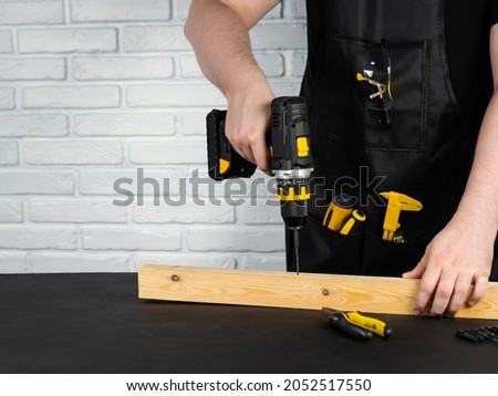 A carpenter drills a hole in a wooden board with an electric drill. Close-up of hands of a foreman at work. Working environment in a carpentry workshop. Cordless cordless drill - screwdriver with dril Royalty-Free Stock Photo #2052517550