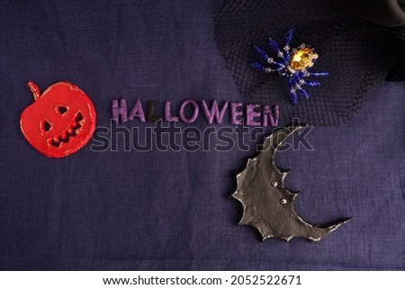 Halloween still life. A black veil, beaded spider, bat, jack-o'-lantern, text - Halloween on a blue background
