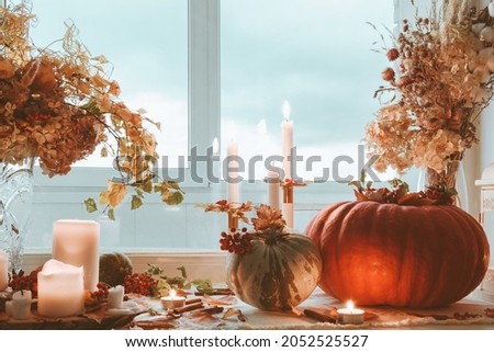 A large orange pumpkin, a small green pumpkin, burning white candles and bouquets on the windowsill. Still life. Autumn, cozy evening at home. Royalty-Free Stock Photo #2052525527