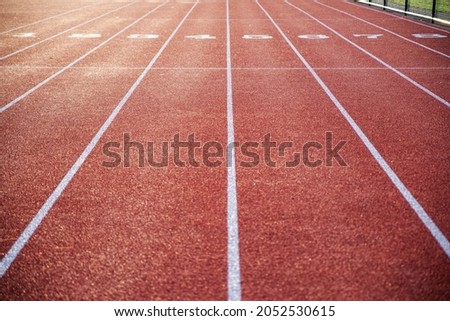 Athletic track in natural light with long numbered lanes to the horizon gives the feeling of preparedness focus and direction, with no people, and copy space Royalty-Free Stock Photo #2052530615