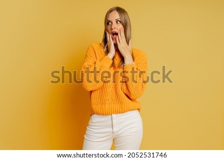 Pretty blond  woman  with suprice face in orange  stylish autumn sweater posing over yellow background in studio. 