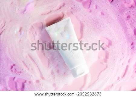 white cosmetic tube on a pink background with soap foam and bubbles. Face or body cleanser concept.  Royalty-Free Stock Photo #2052532673