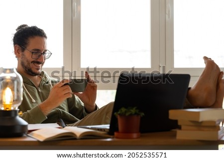 Medium shot of male smiling at his phone with feet on the table Royalty-Free Stock Photo #2052535571