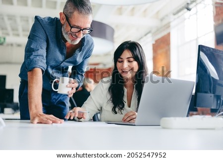 Two happy colleagues collaborating on a new project in the office. Mature businessman teaming up with his female colleague in a modern office. Two colleagues smiling while working together. Royalty-Free Stock Photo #2052547952