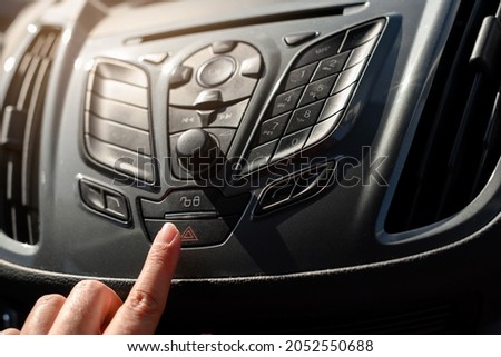 Finger on the red triangle button of a car's hazard warning lights panel