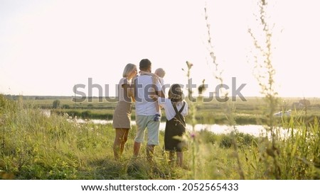 Happy family near the lake at the day time. Concept of friendly family. Husband and wife stand by the lake in the evening. They hold their children in their arms and look into the distance, only the