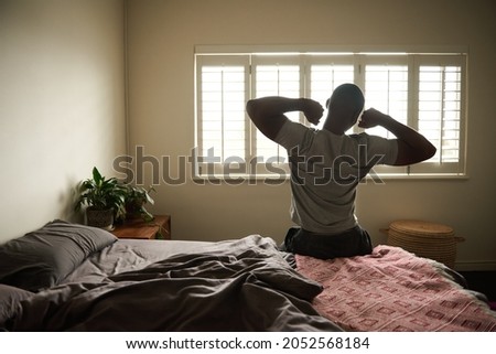 Young African man stretching on his bed in the morning Royalty-Free Stock Photo #2052568184