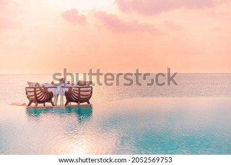 Summer love and romance table set-up for a romantic dinner meal with infinity pool reflection chairs under sunset sky and sea in the background. Luxury destination dining, romantic dinner for couples Royalty-Free Stock Photo #2052569753