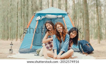 Group of young asia camper friends camping near relax enjoy moment in forest. Female traveler using smartphone taking selfie at campsite. Outdoor activity, adventure travel, or holiday vacation.