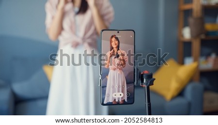 Happy young Asian girl blogger front of phone camera record video enjoy with dance content in living room at home. Social distance coronavirus pandemic concept. Freedom and active lifestyle concept Royalty-Free Stock Photo #2052584813