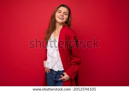 Photo of beautiful young woman with long dark hair standing wearing white t-shirt and red cardigan isolated over red background looking at camera smiling and poising hands in jeans pockets Royalty-Free Stock Photo #2052596105