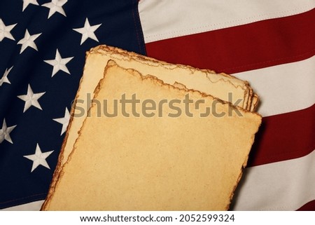 Close up heap of blank vintage yellow paper sheets on old weathered cotton embroidered US national flag, symbol of American history, elevated high angle view, directly above