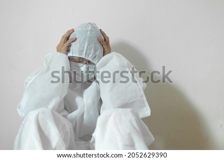 A doctor in a white protective uniform feels tired. Coronavirus
