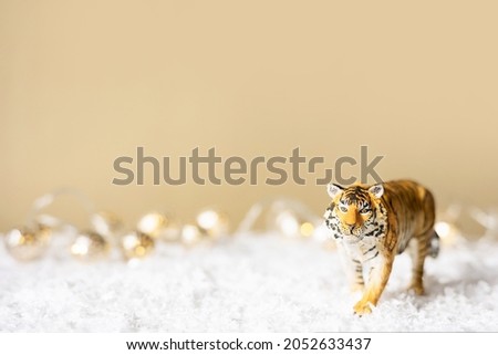 Figurine of tiger in snow on beige background. Tiger symbol of the Chinese new year 2022. Christmas greeting card. Copy space