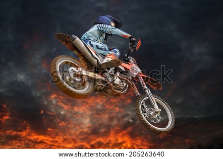 Jumping motocross rider with firestorm in the background and red glowing spinning rear wheel