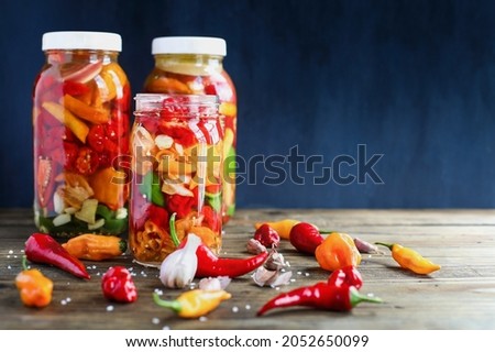 Variety of peppers, spices and garlic in a mason jars fermenting, a rich source of probiotics, to make homemade hot sauce over a rustic wood background table. Selective focus with blurred background.