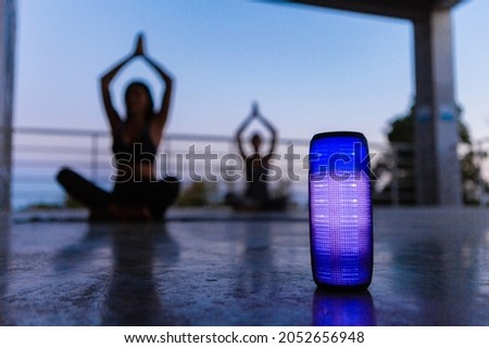 colorful backlight wireless speaker on foreground of company of friends doing yoga listening to music in dusk