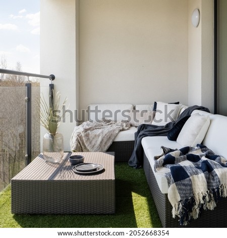 Stylish balcony with fake grass and comfortable, rattan corner sofa with pillows and blankets and square coffee table Royalty-Free Stock Photo #2052668354