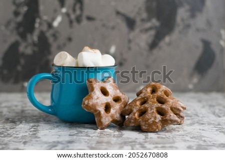 Christmas cookies and coffee with marshmallows and cinnamon in a blue cup on a light gray background.