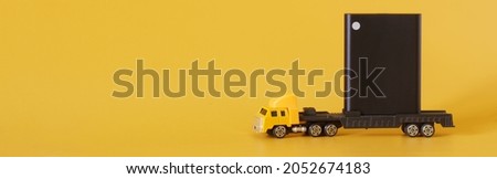 Toy truck carries a small External portable SSD. Solid State Drive. The concept of modern technologies, gadgets and storage of information on an SSD disk. Web banner. Free space for an inscriptio