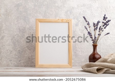 White wooden frame mockup with lavender in ceramic vase and linen textile on gray concrete background. Blank, vertical orientation, still life.