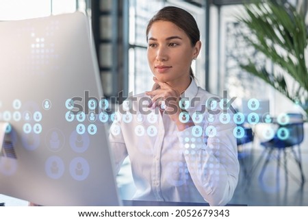 Attractive businesswoman in white shirt at workplace working with laptop to hire new employees for international business consulting. HR, social media hologram icons over office background Royalty-Free Stock Photo #2052679343