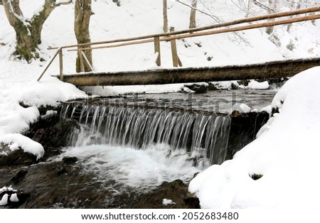 pedestrian wooden bridge over mountain stream in winter Carpathians during snowfall, Ukraine
