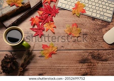 Coffee cup, vintage books, glasses and autumn maple leaves on wooden table.