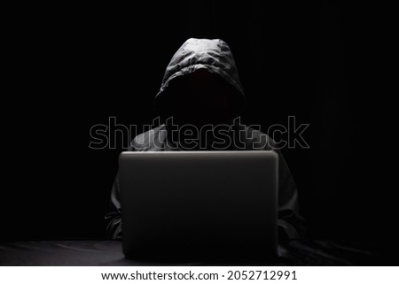 Hackers wear hoods to cover their faces. Hacking to steal important information. Use a computer to release malware viruses Ransom and harass organizations. He sitting in the dark room with neon light Royalty-Free Stock Photo #2052712991