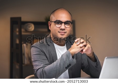 Young asian businessman working with laptop computer in the dark office at night. Attractive handsome Indian man work hard overtime in home with floor lamp ambient warm light late at night