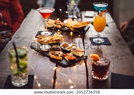 Blurred background of multicolored drinks and minimal food - Happy hour concept with fancy cocktails and tasty appetizers served at rooftop lounge prive - Warm vintage filter on shallow depth of field Royalty-Free Stock Photo #2052736358