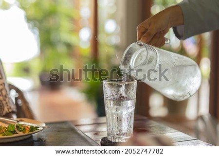 Waiter hand pouring water with ice into glasses on table Royalty-Free Stock Photo #2052747782