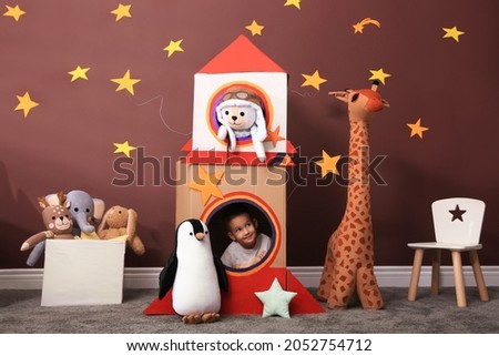 Cute little boy playing with cardboard rocket and toys at home. Child's room interior