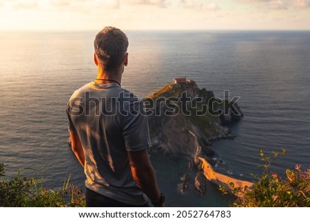 Young caucasian woman looking to Gaztelugatxe ermitage at Basque Country coast.