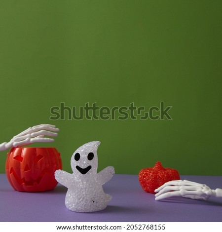 Pumpkins for Halloween with a ghost on a purple background with hand bones with copy space on a green background. Minimal aesthetic concept.